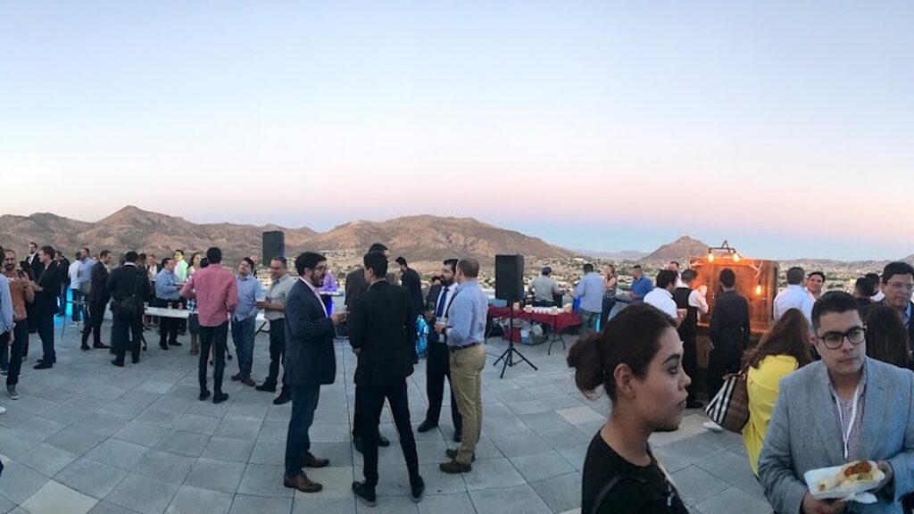 Founders and guests networking on a rooftop terrace at dusk in Chihuahua, with the sierra and city skyline behind them